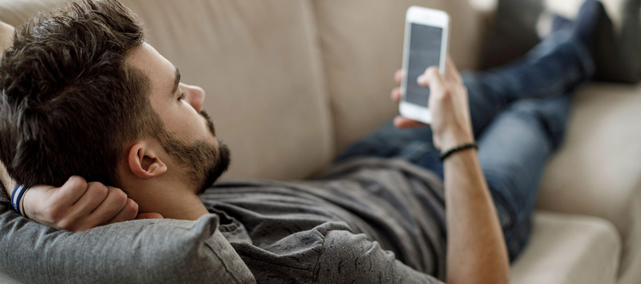 man lying down on couch with his phone